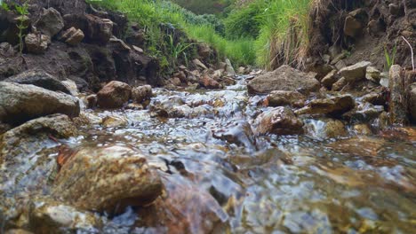 Low-angle-surface-pov-of-small-narrow-water-stream-in-woods-running-through-rocks