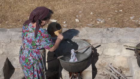 A-woman-pours-hot-water-into-a-xartzin-or-copper-boiler-during-a-historical-re-enactment-of-washing-clothing-as-they-did-in-the-1900s-in-Kritou-Terra,-Greece