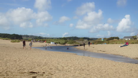 People-Relax,-Walk,-And-Swim-In-The-Red-River-on-Marazion-Beach-on-Sunny-Summer-Day,-Cornwall