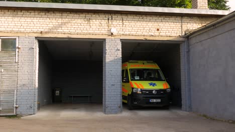 Yellow-paramedic-ambulance-vehicle-parked-inside-the-white-brick-garage,-sunny-day,-wide-shot