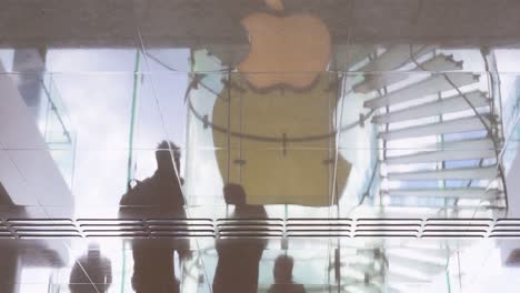 Reflexion-Von-Käufern,-Die-An-Dem-Amerikanischen-Multinationalen-Technologieunternehmen-Apple-Store-Vorbeigehen,-Und-Das-Logo,-Das-Sich-Auf-Dem-Boden-In-Hongkong-Widerspiegelt