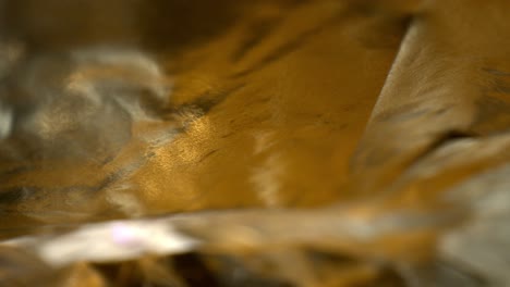 Pushing-towards-top-layer-of-contoured-textured-colorful-foil-with-yellow-and-gold-coloring,-macro-view-of-the-foil-as-it-moves-and-flows