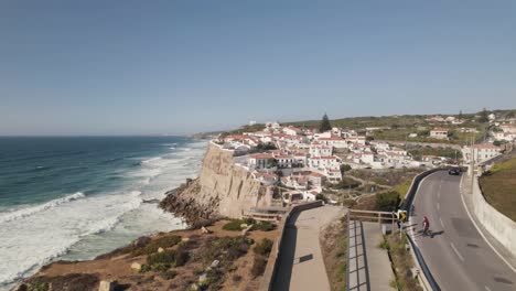 People-walking-on-walkway-along-seaside-cliff,-coastal-road-near-Azenhas-do-Mar,-Portugal