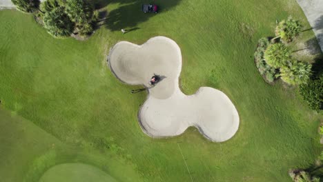 Aerial-drone-shot-of-golf-course-bunker-being-raked-by-landscaping-crew