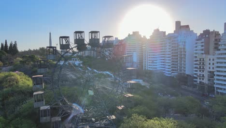 Drone-flyover-rustic-ferries-wheel-reveals-stairway-lookout-platform-with-sun-glowing-in-the-background-and-rows-of-buildings-on-the-side-and-traffic-crossing-on-poeta-leopoldo-lugones-avenue