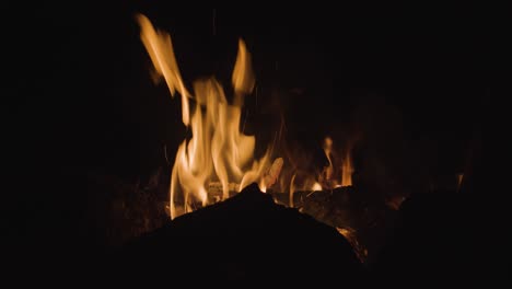 Ein-Warmes-Lagerfeuer-Brennt-Nachts-Hell-Mit-Der-Silhouette-Von-Felsen-Davor