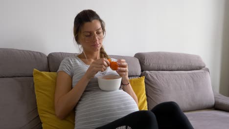 Beautiful-pregnant-woman-with-glasses-peals-tangerine-and-eats-it