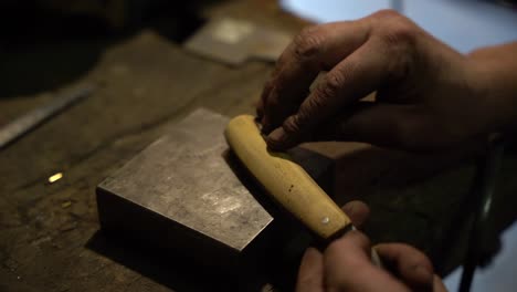 Sanding-knife-blade-handle-by-hand-with-sandpaper-by-hand,-Close-up-handheld-shot