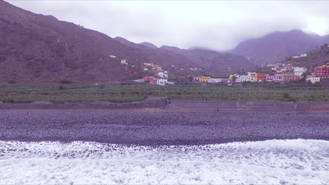 Vista-Aérea-De-La-Playa-De-Hermigua,-Valle,-Plantación-De-Plátanos,-Casas-Coloridas-Y-Montañas-En-El-Valle-De-Hermigua,-Al-Norte-De-La-Gomera,-Islas-Canarias,-España-En-Un-Día-Nublado
