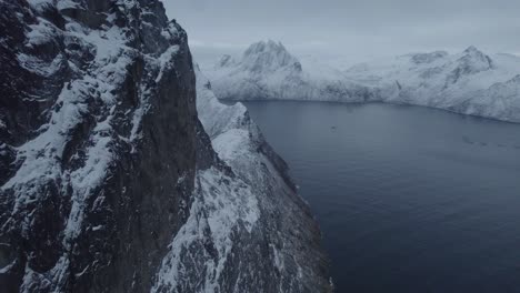 Aerial-view-close-to-the-snowy-Segla-mountain-wall,-high-above-sea,-winter-in-Senja,-Norway---tilt,-drone-shot