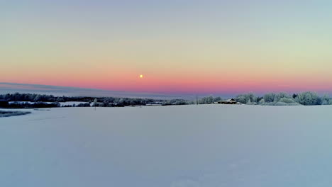 Aerial-flight-towards-full-moon-at-colorful-sky-early-in-the-morning-during-white-snowy-winter-day-in-Nature