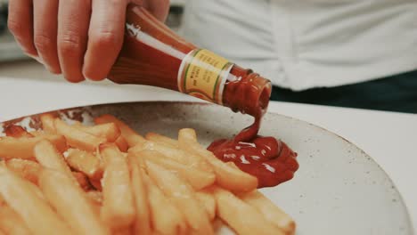 Chef-puts-deep-red-color-ketchup-onto-plate-with-golden-french-fries