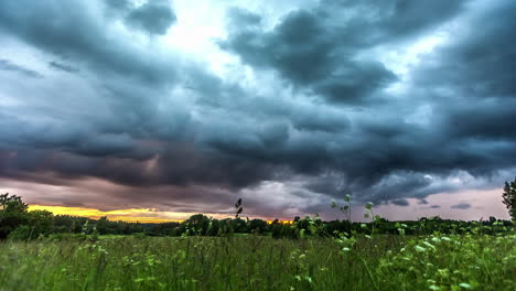 Ominous-dark-storm-clouds-over-field-at-sunset,-dissipates-again