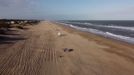Aerial-view-showing-family-parking-car-at-the-sandy-beach-during-holidays-and-enjoying-ocean-vibes-during-sunset