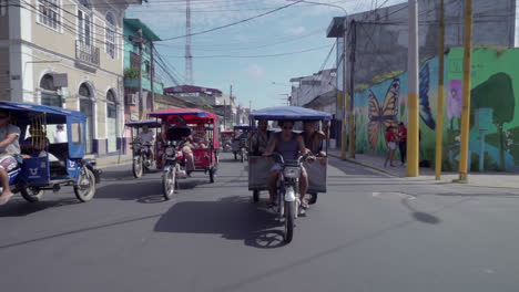 Trike-taxis-drive-down-busy-street-in-Iquitos,-Peru-on-a-sunny-day