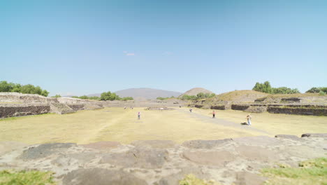 Wide-shot-of-pre-Columbian-Teotihuacan-Pyramids-site-in-Mexico-with-tourists-in-the-distance-on-a-sunny-day