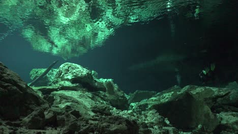 Scuba-diver-reaching-the-exit-of-Cenote-cave-system-Tajma-Ha-in-Yucatan-Mexico-with-rock-formations-reflecting-on-water-surface