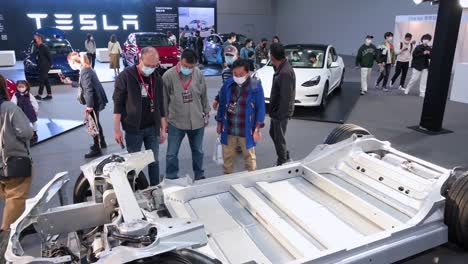 Visitors-look-and-test-at-a-Tesla-Motor-chassis-car-and-vehicle-frame-of-a-motor-vehicle,-during-the-International-Motor-Expo-showcasing-EV-electric-cars-in-Hong-Kong