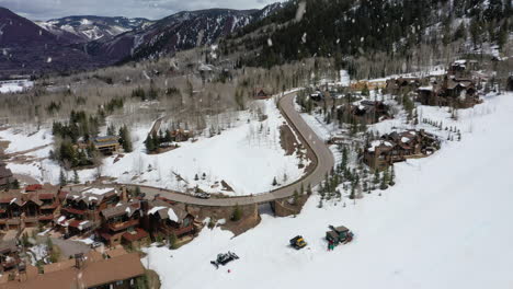 Mountain-skiing-resort-town-and-people-sliding-downhill,-aerial-fly-over-view-during-snowfall