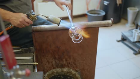 Glassmith-heats-glassware-with-flame-torch-in-workshop