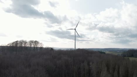 Wind-turbine-spinning-fast-behind-a-dark,-dry-forest-in-western-Germany