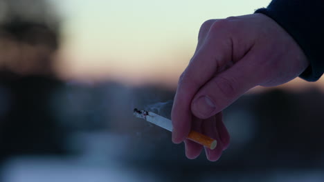 Close-up-of-male-caucasian-hand-holding-a-lit-cigarette-outdoors