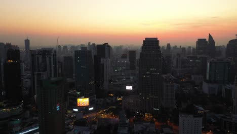 Aerial-rising-overlooking-skyline-and-outlines-of-skyscrapers-of-Sukhumvit-district-during-colorful-red-sunrise-in-Bangkok,-Thailand