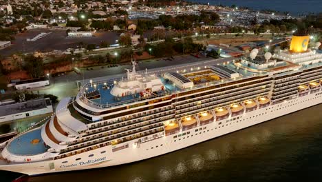 Aerial-flyback-over-Costa-Deliziosa-luxury-cruise-ship-moored-in-Sans-Souci-port-at-sunset,-Santo-Domingo