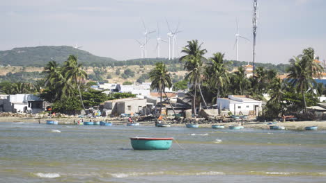 Static-shot-of-beach-scene-with-moored-coracle-boat,-wind-turbines-in-background