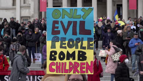 A-placard-painted-the-blue-and-yellow-colours-of-the-Ukrainian-flag-reads,-“Only-evil-people-bomb-children”-on-protest-in-Trafalgar-Square-opposing-the-Russian-invasion-of-Ukraine