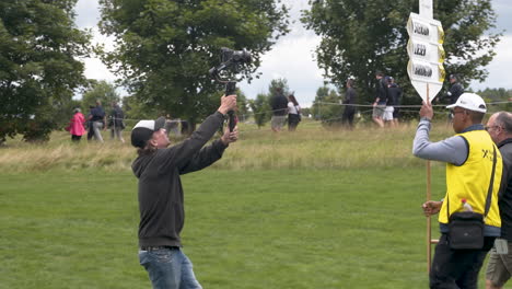 Cameraman-recording-a-man-carrying-a-scoreboard-at-a-golf-tournament