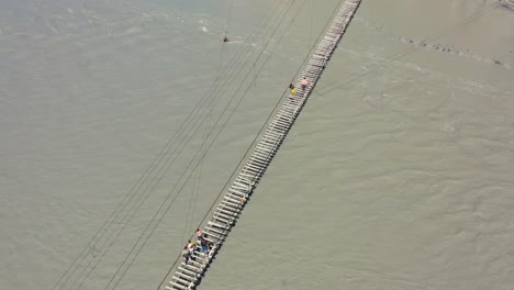 Luftaufnahme-Von-Oben-Nach-Unten-Von-Touristen,-Die-Vorsichtig-Die-Berühmte-Gefährliche-Hussaini-Brücke-über-Einen-Schnelllebigen-Grauen-Fluss-In-Hunza-Pakistan-überqueren