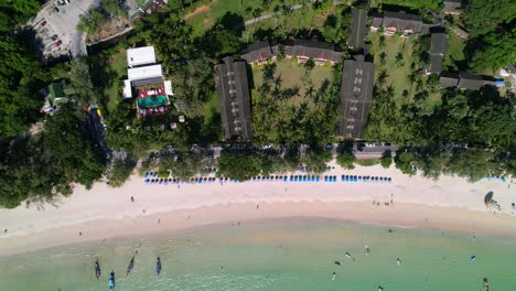 Blick-Von-Oben-Nach-Unten-Auf-Blaue-Sonnenschirme-Und-Ein-Resort-An-Einem-Tropischen-Karon-Strand-Mit-Weißem-Sand,-Türkisblauem-Wasser-Und-Booten,-Die-In-Phuket,-Thailand,-Verankert-Sind