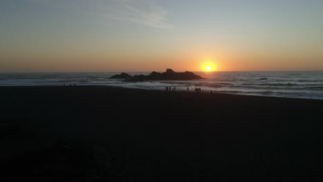 Sonnenuntergang-Im-Ozean-Mit-Silhouettierten-Menschen,-Die-Auf-Der-Strandantenne-Spazieren-Gehen