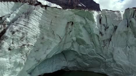 Gran-Glaciar-En-Los-Alpes-Italianos-Con-Cueva-Y-Lago-Verde-Glacial,-Toma-Aérea-De-Abajo-Hacia-Arriba