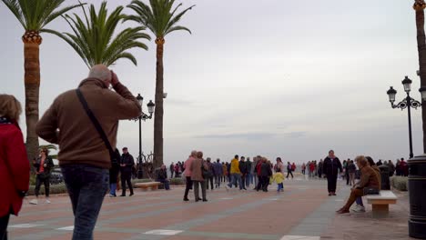 Crowds-of-people-walking-across-a-typical-European-promenade-with-palm-trees