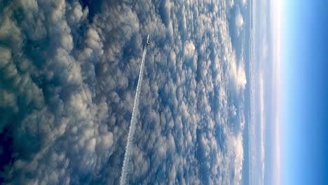 Flying-airplane-above-clouds-leaving-condensation-vapor-air-trail-in-blue-sky