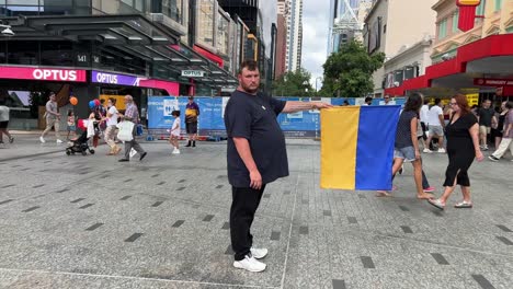 Silence-male-peaceful-demonstrator-standing-in-the-middle-of-Queen-Street-Mall,-Brisbane,-holding-a-Ukrainian-national-flag-to-show-support-and-raise-awareness-of-Russian-invasion-crisis-in-Ukraine