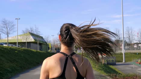 Fit-young-woman-running-outdoors-tracking-shot-behind