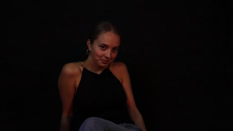 Confident-teenage-girl-flirting-while-sitting-in-front-of-a-black-background