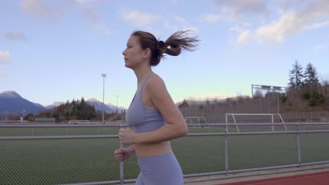 Mixed-Race-Asian-Woman-Jogging-on-Track,-Slow-Motion-Profile-Following