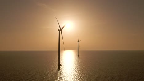 Wind-turbines-silhouette-spinning-over-water,-Windpark-at-sunset,-Aerial-Pullback
