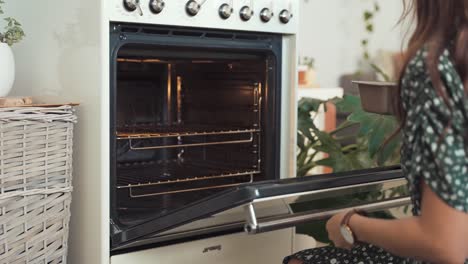 Slow-motion-shot-of-a-woman-dressed-in-a-green-dress-placing-a-cake-into-a-white-oven