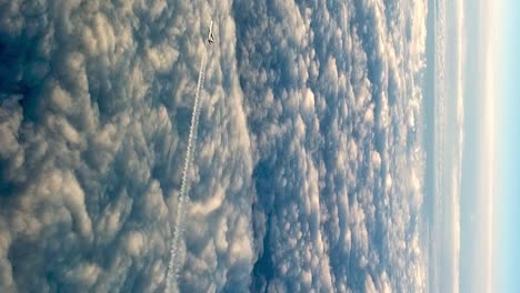 Aerial-video-of-plane-flying-above-clouds,-leaving-vapor-trail-in-blue-sky