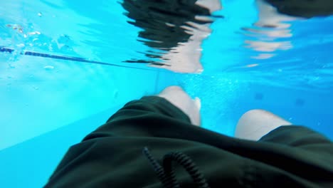 Under-water-man's-legs-inside-an-outdoor-swimming-pool-with-blue-mosaic-walls