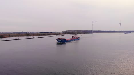 Aerial-Dolly-Forward-Over-Oude-Maas-With-Still-Wind-Turbines-And-Torpo-Cargo-Ship-Approaching-In-Distance-On-Cloudy-Day