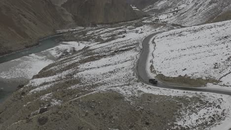 Aerial-Drone-View-Of-Black-SUV-Driving-Winding-Snow-Rocky-Mountain-Roads-In-Winter-Through-Hunza-Valley