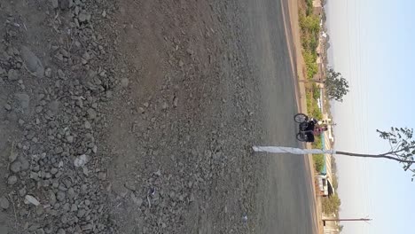 A-close-up-vertical-video-shot-Of-a-Biker-riding-a-bike-on-the-unconstructed-road