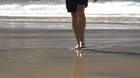 Man-walking-in-the-beach-in-slowmotion-showing-bare-feet-stepping-into-sand