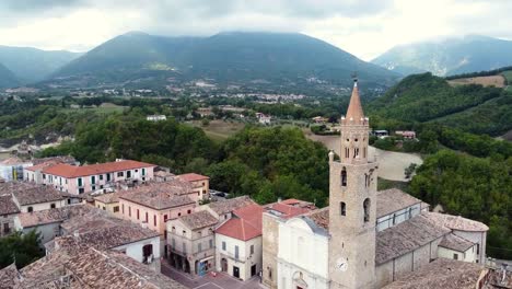 Aerial-ascending-view-of-a-bell-tower-in-a-small-Italian-town-in-a-mountain-landscape